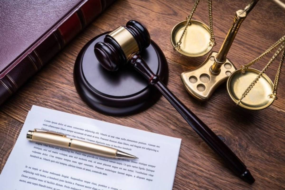 Gavel, scales and document with a gold pen rest on a wooden table.