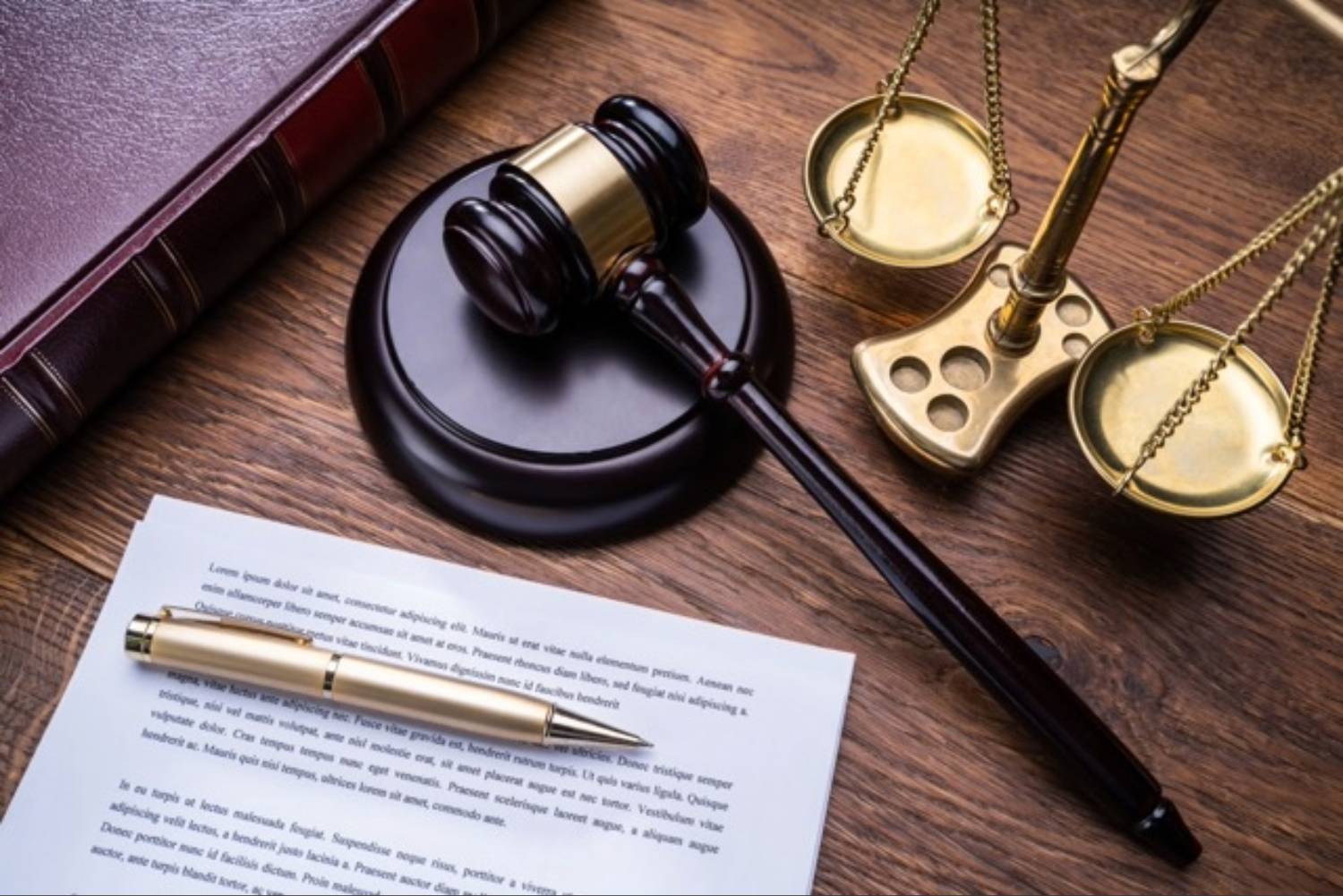 Gavel, scales and document with a gold pen rest on a wooden table.