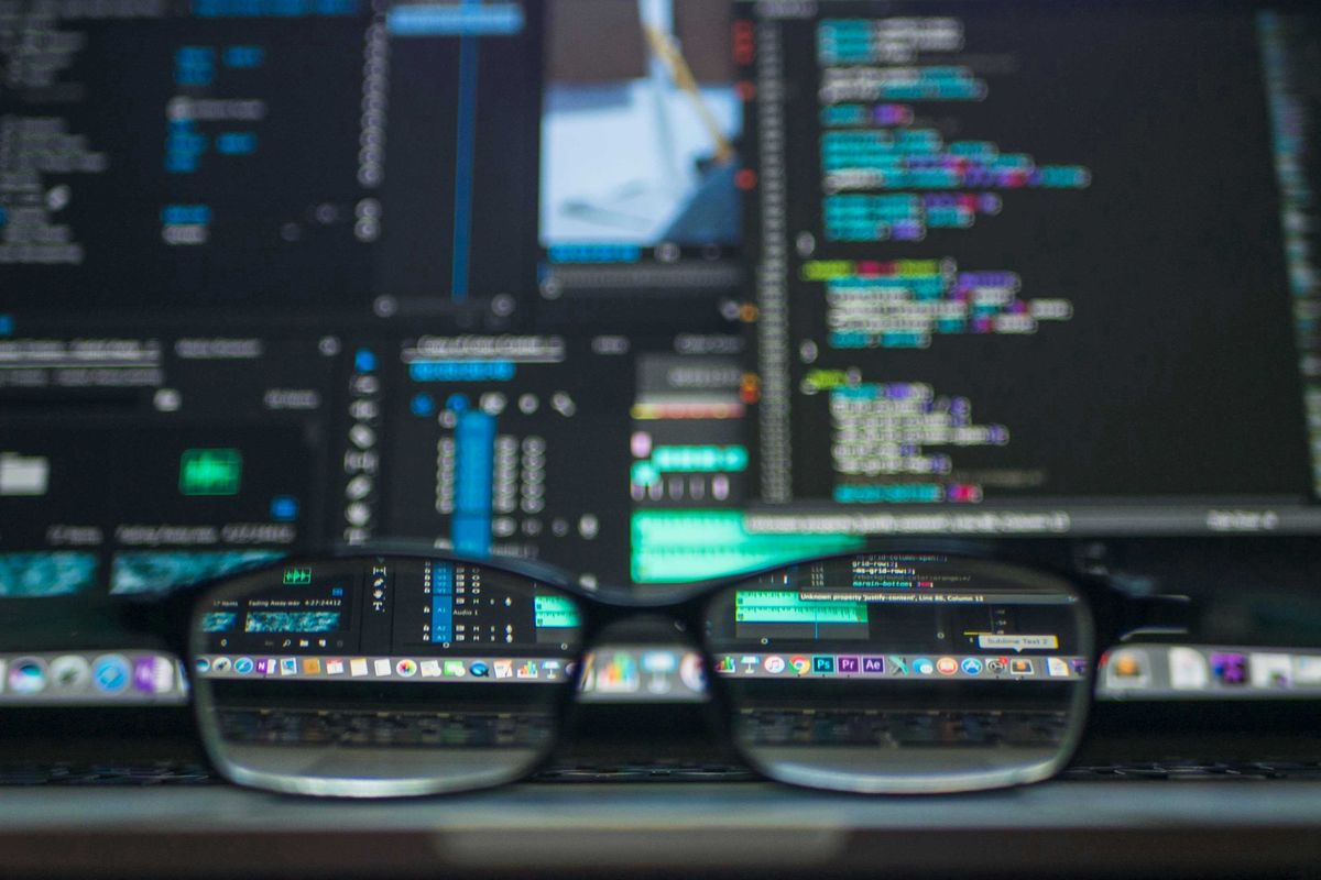 Glasses on a laptop keyboard with blurry code on the screen in the background.
