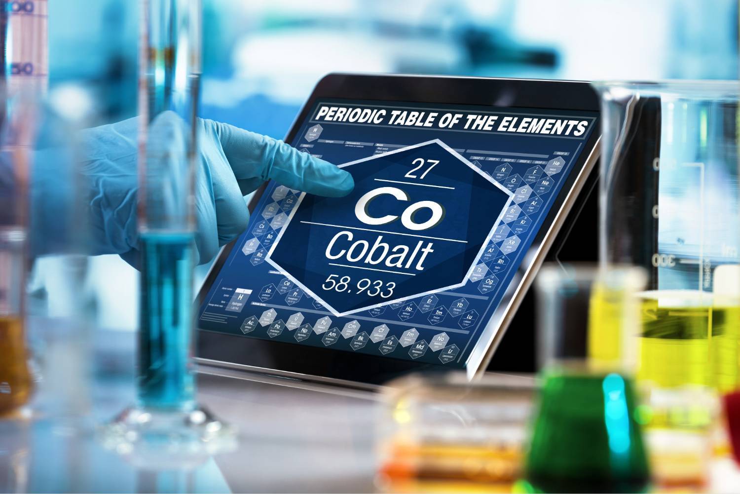 Gloved hand selecting cobalt on a digital periodic table, surrounded by lab equipment.