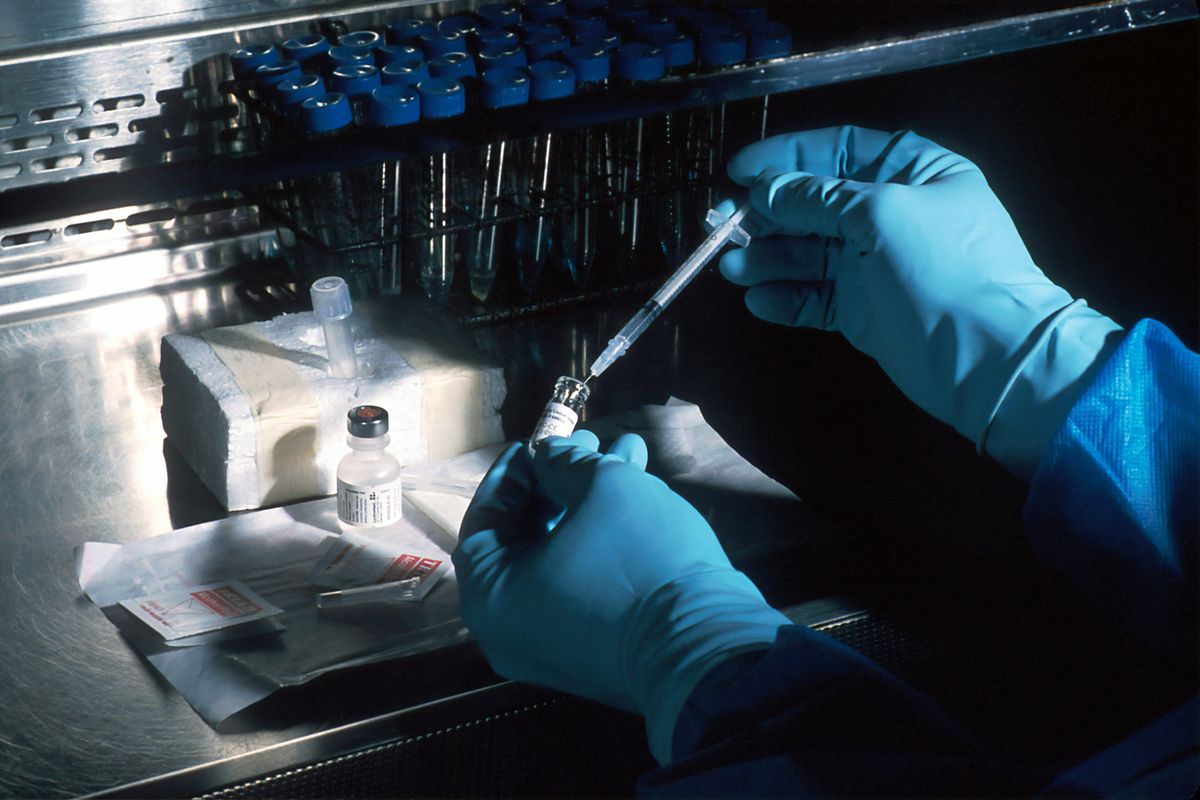 Gloved hands preparing a syringe with a vial in a lab setting.