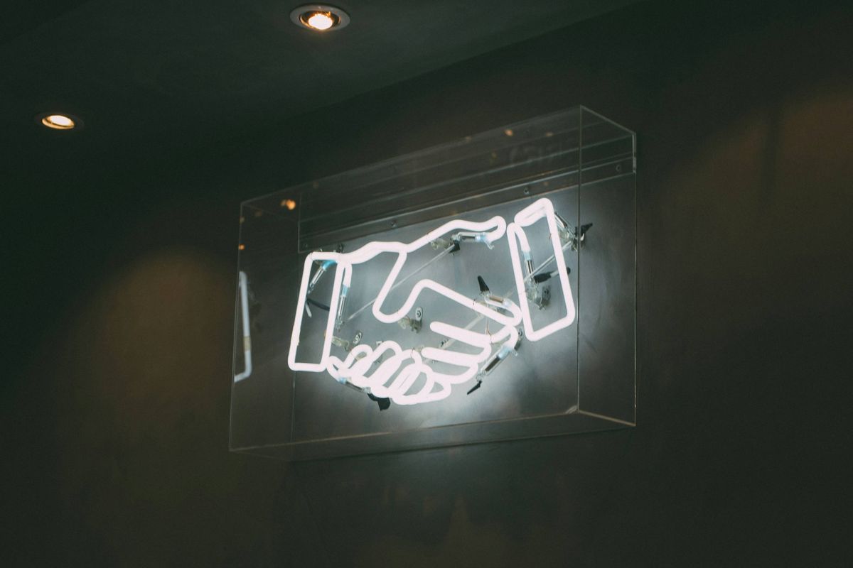 Glowing neon handshake sign on a dark wall.