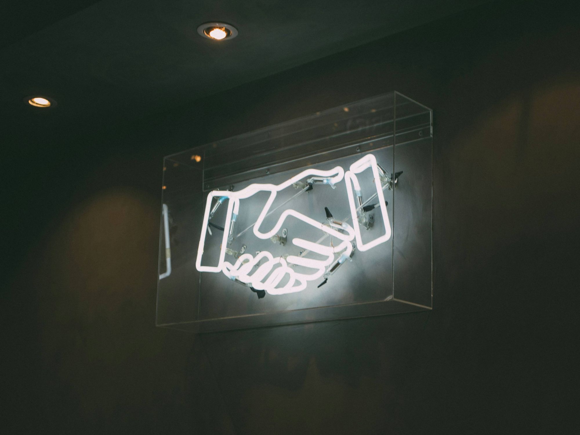 Glowing neon handshake sign on a dark wall.