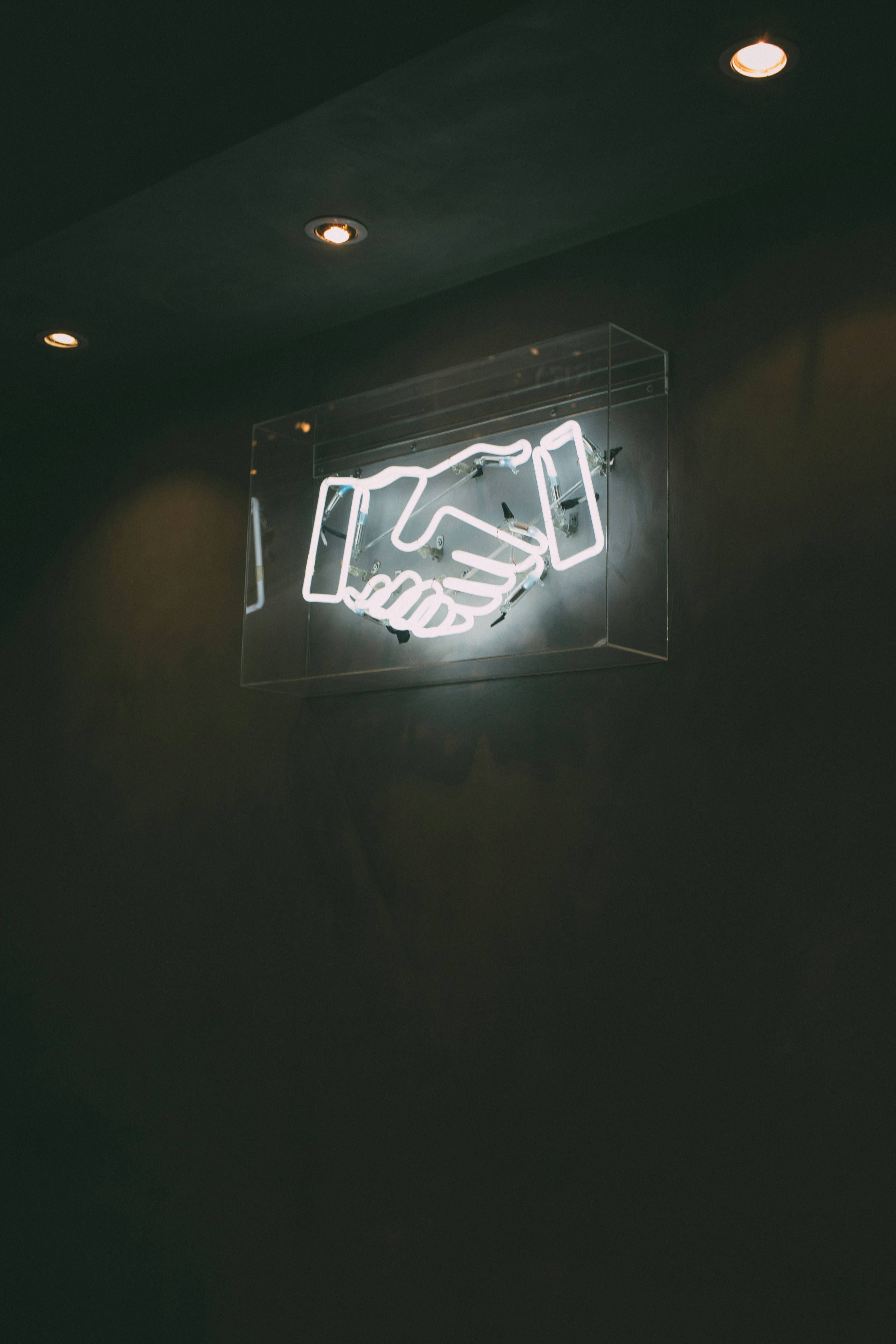 Glowing neon handshake sign on a dark wall.