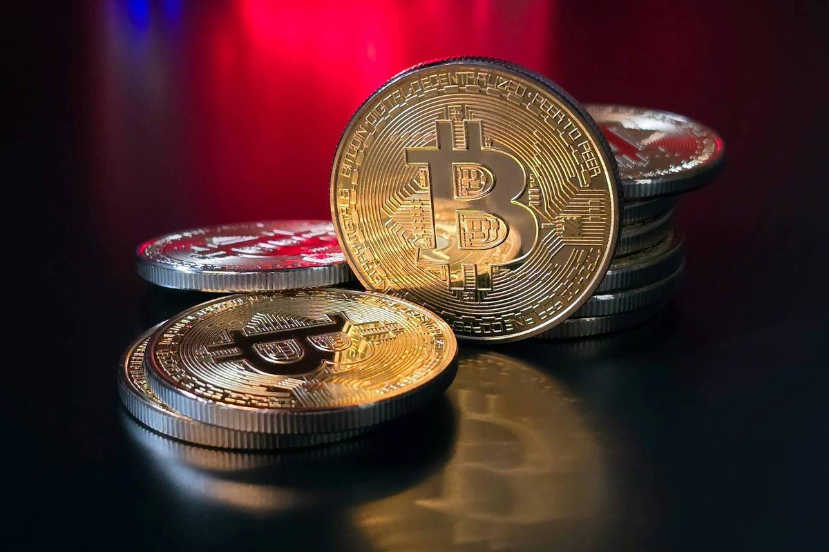 Gold and silver Bitcoin coins stacked on a reflective black surface with red and blue lights in the background.