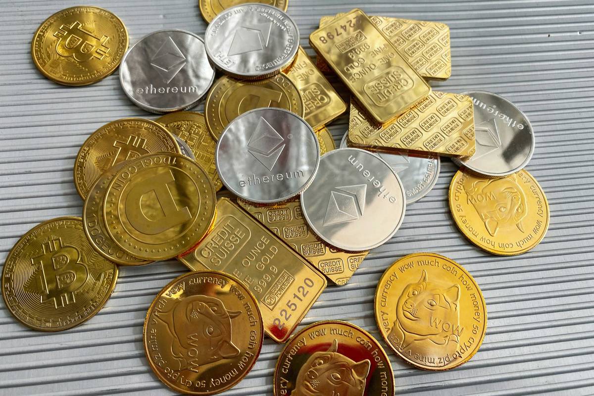 Gold and silver crypto coins and gold bars on a striped surface.