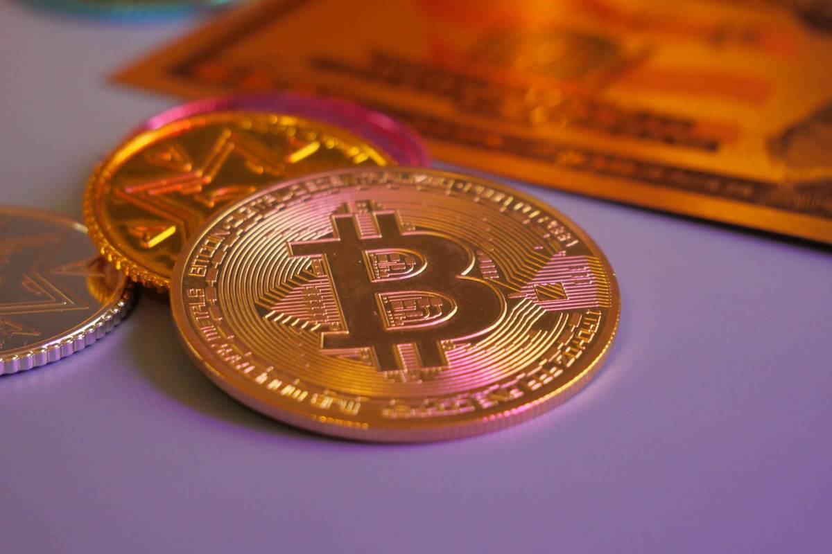 Gold and silver cryptocurrency coins rest on a reflective surface.