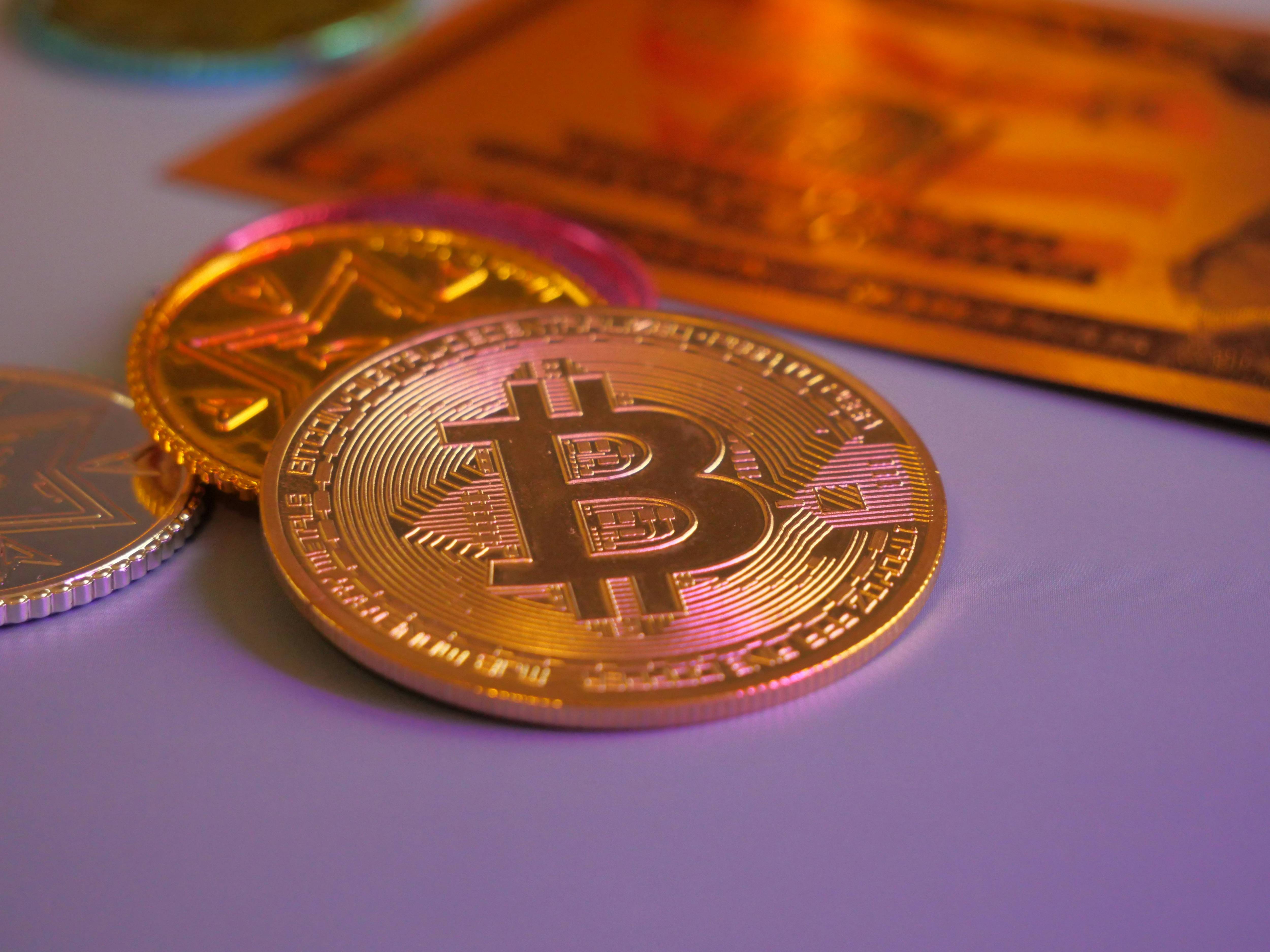 Gold and silver cryptocurrency coins rest on a reflective surface.