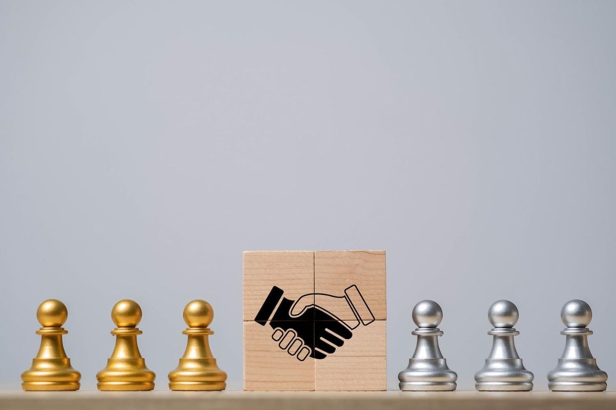 Gold and silver pawns flank wooden blocks with a handshake illustration.