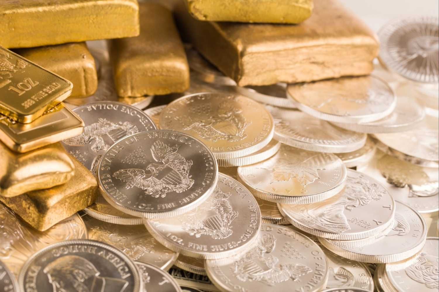 Gold bars and silver coins scattered on a surface.