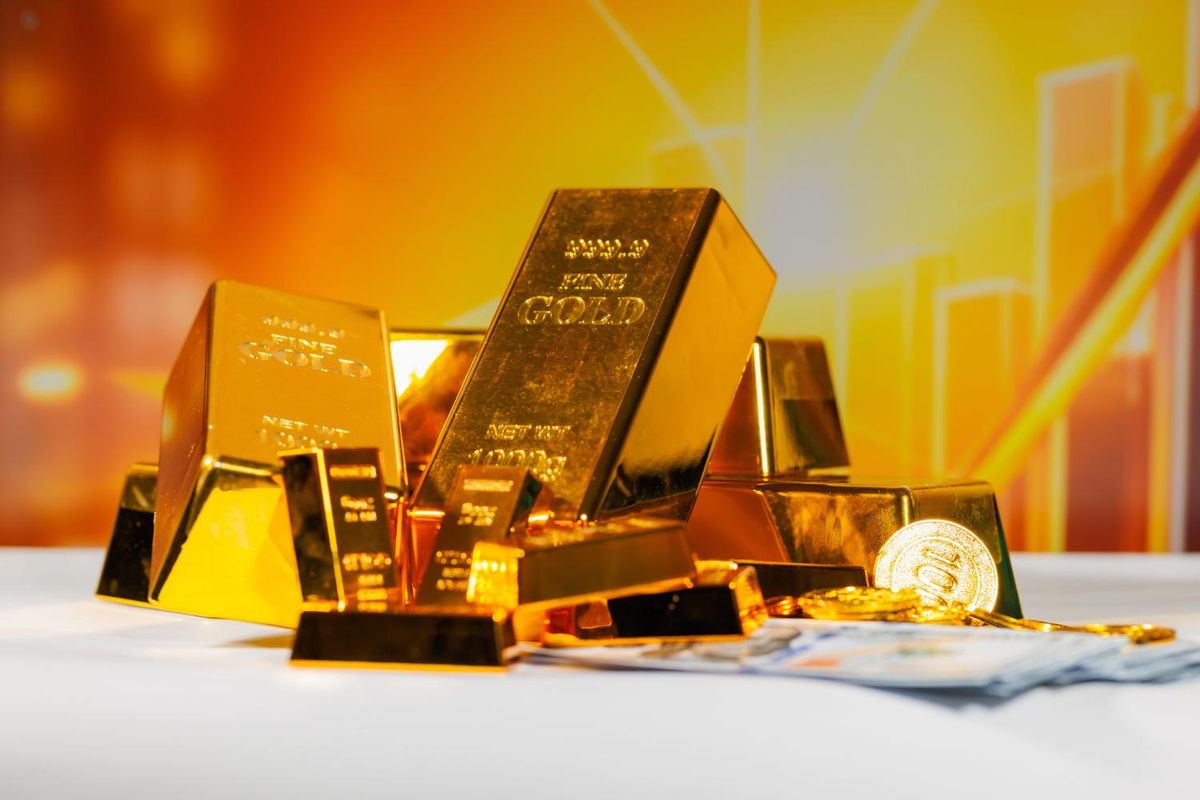 Gold bars, coins and currency on a table with a warm background.