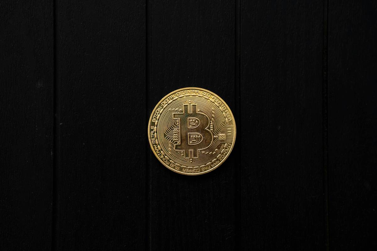 Gold Bitcoin coin rests on a black wood background.