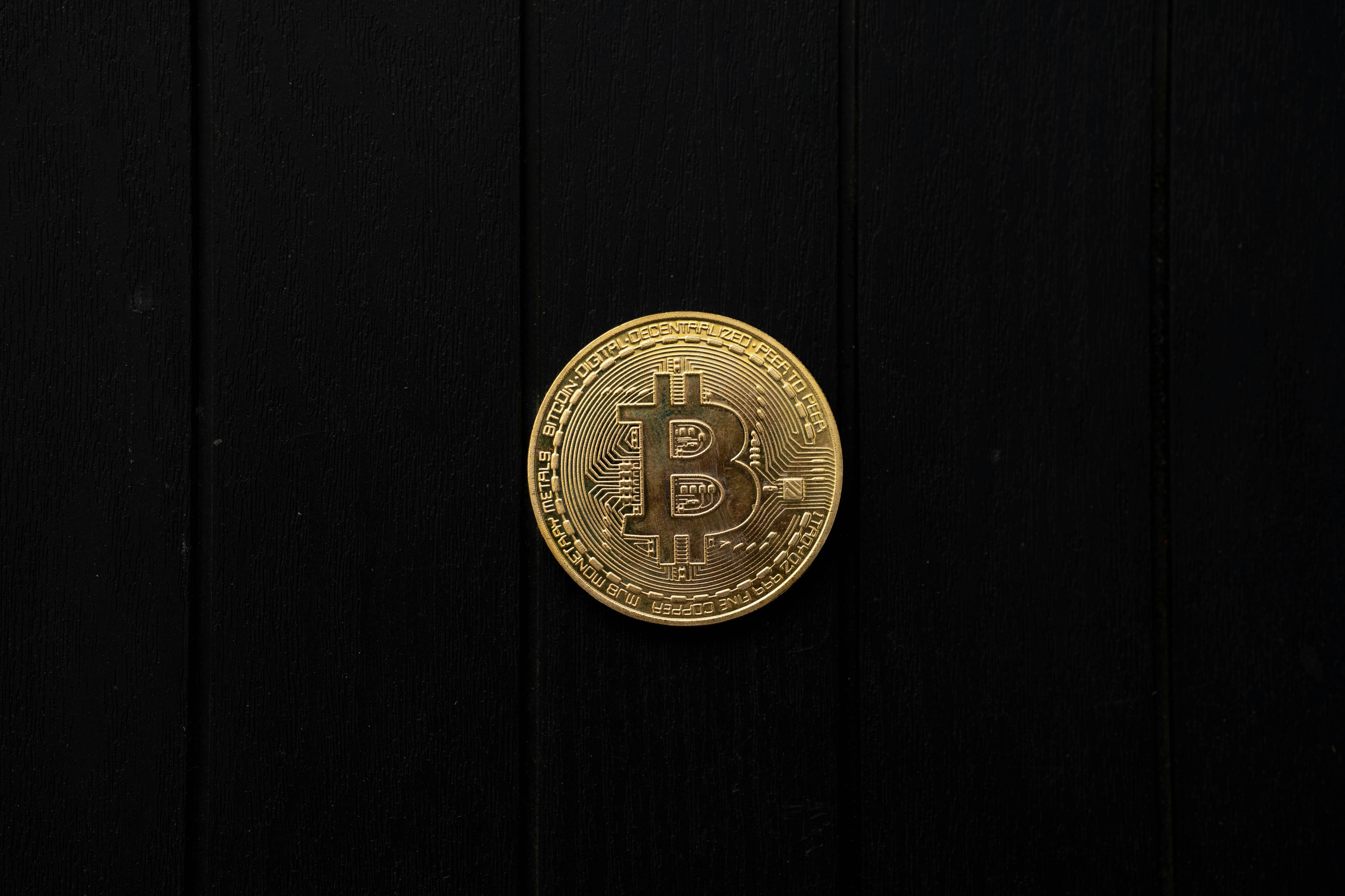 Gold Bitcoin coin rests on a black wood background.