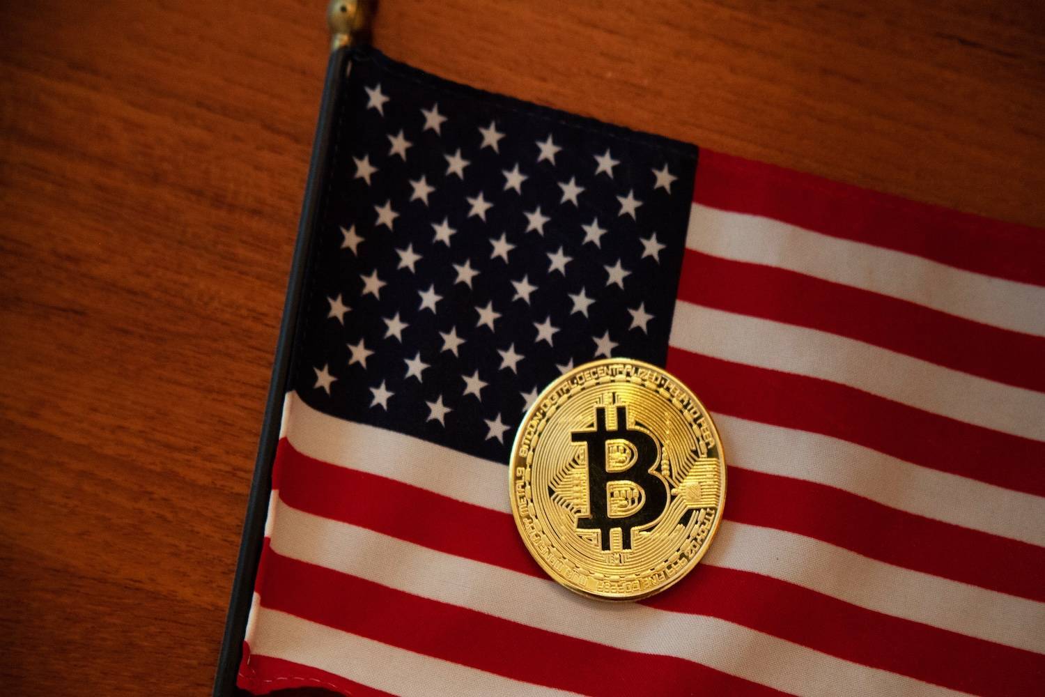 Gold Bitcoin coin rests on an American flag laid on a wooden surface.