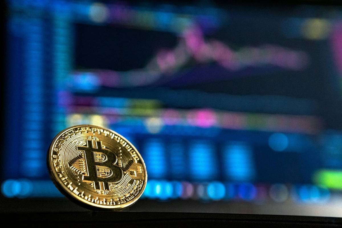 Gold Bitcoin in front of colorfully lit computer screen showing graphs and data.