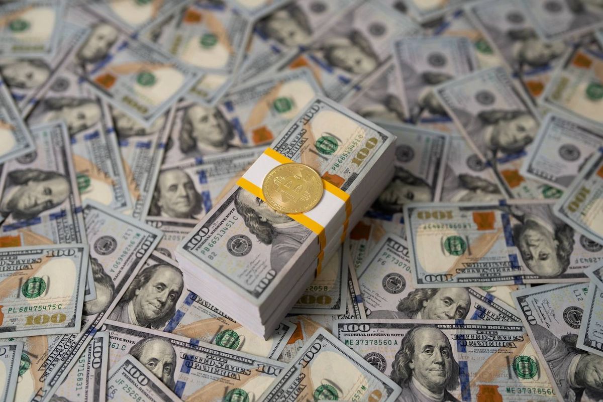 Gold Bitcoin on stack of 100-dollar bills among scattered banknotes.