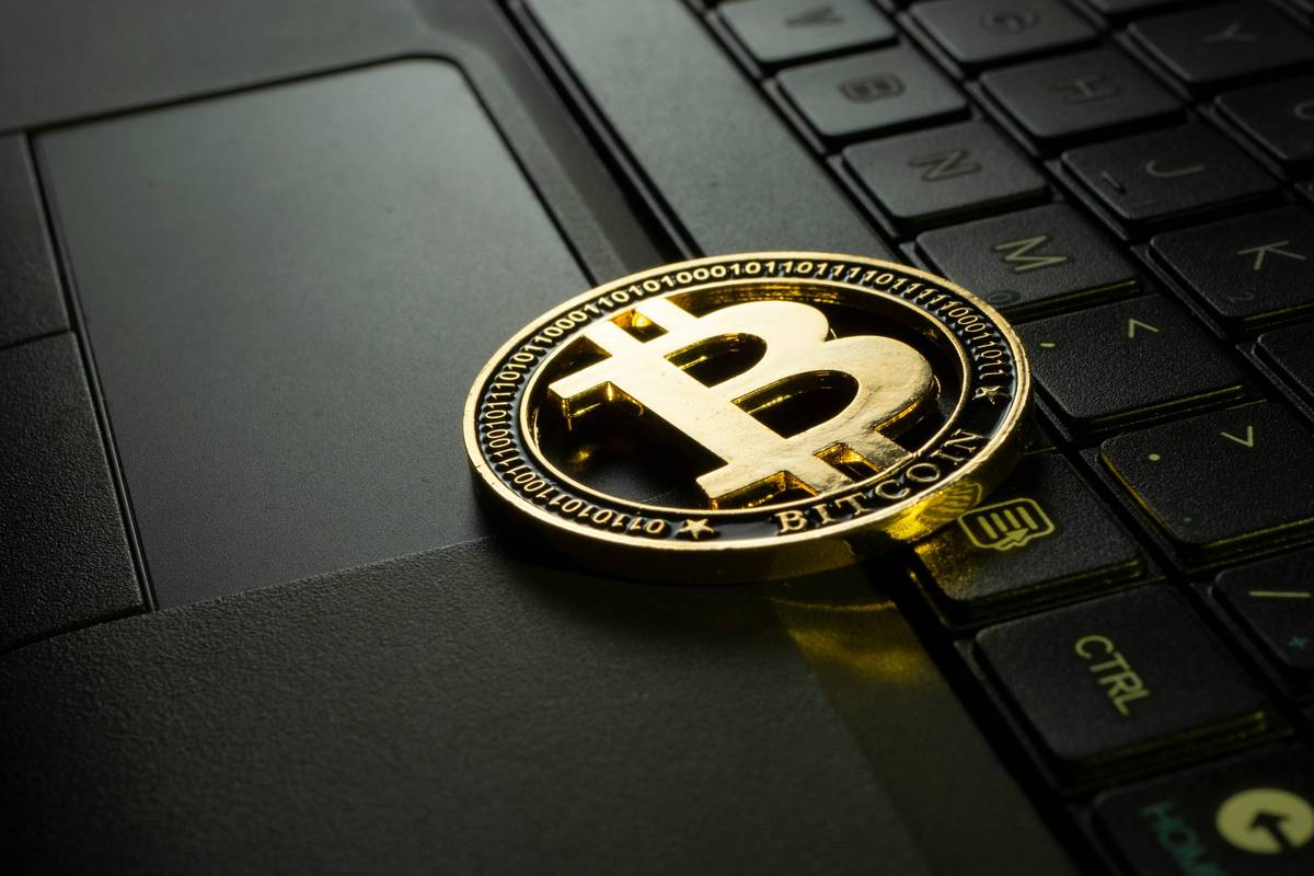 Gold Bitcoin rests on a laptop keyboard partially covering the trackpad.