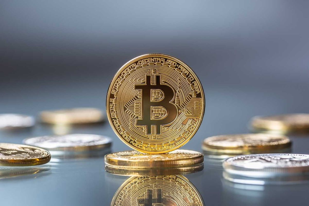 Gold Bitcoin standing among other coins on a reflective surface.