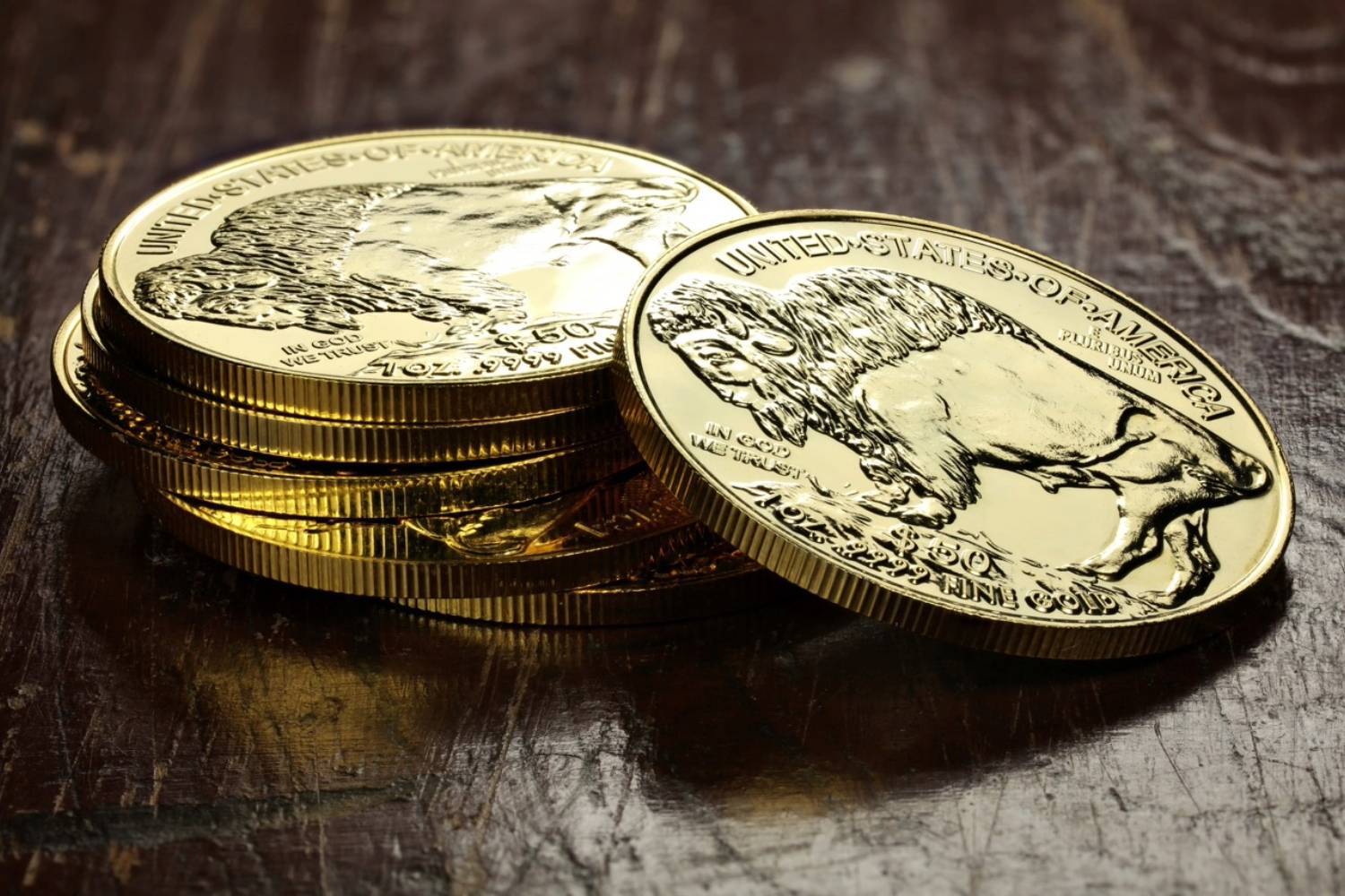 Gold coins featuring a buffalo design stacked on a dark wooden surface.