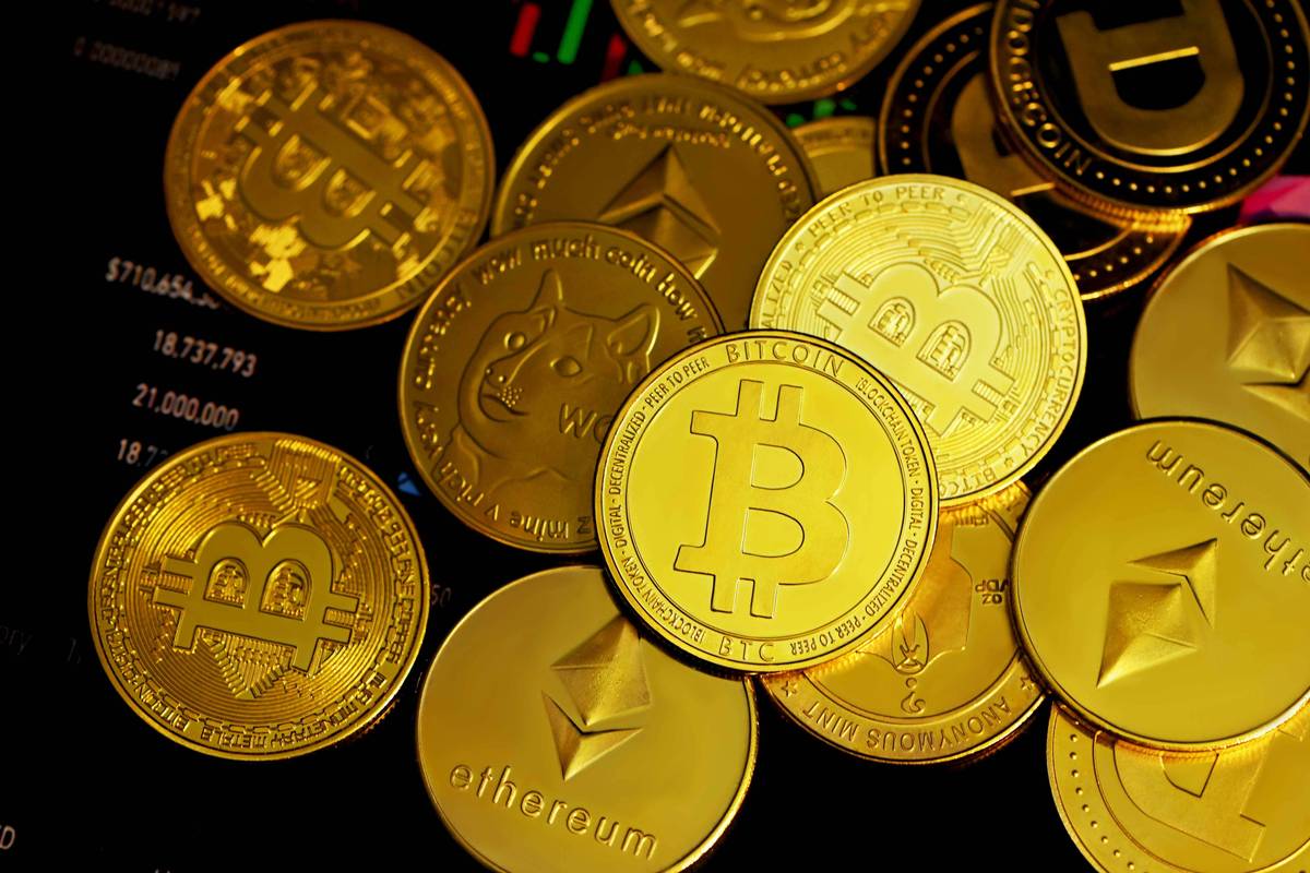 Gold cryptocurrency coins featuring Bitcoin, Ethereum, and Dogecoin logos are piled on a dark digital chart background.