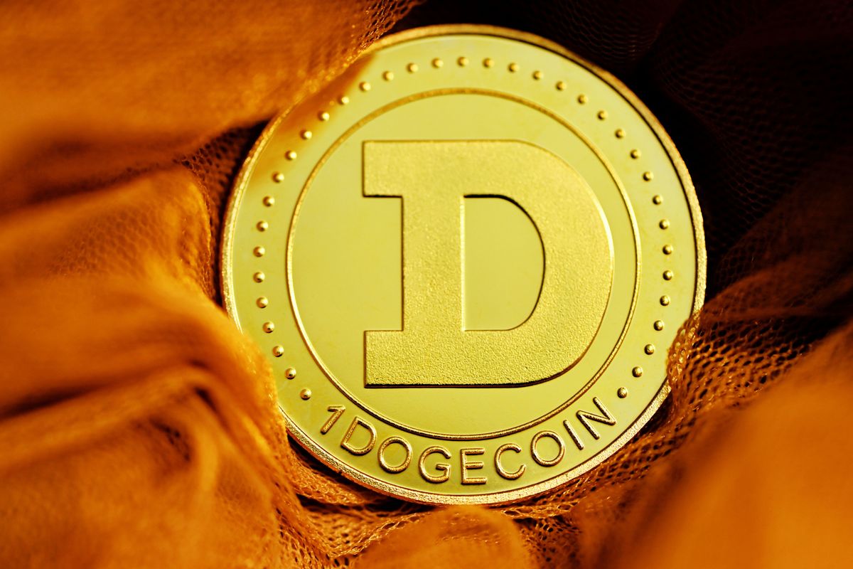 Gold Dogecoin coin with "D" symbol on an orange fabric background.