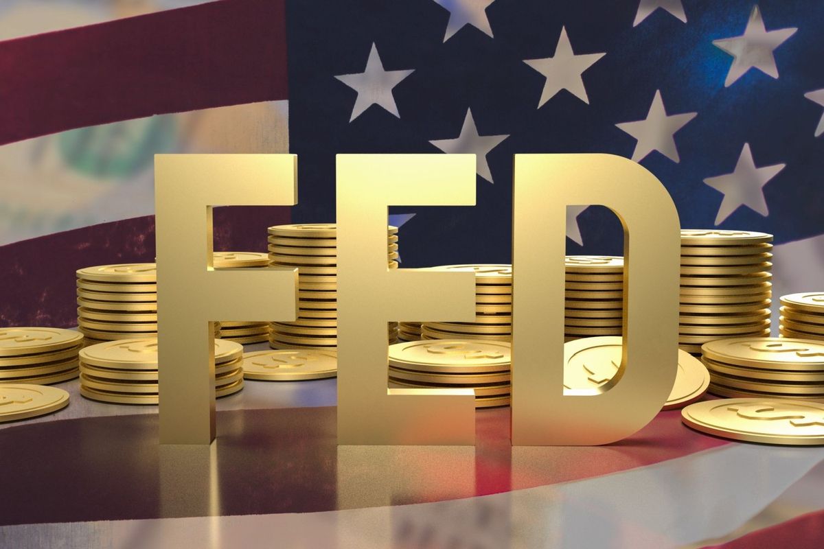 Gold letters spelling FED in front of a pile of gold dollar coins and the US flag.