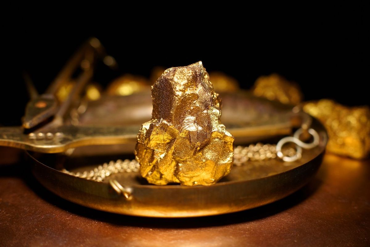 Gold nugget displayed on an antique balance scale with a dark background.