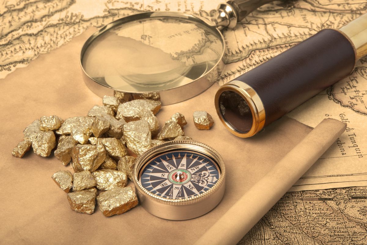 Gold nuggets on top of a map beside a compass. 