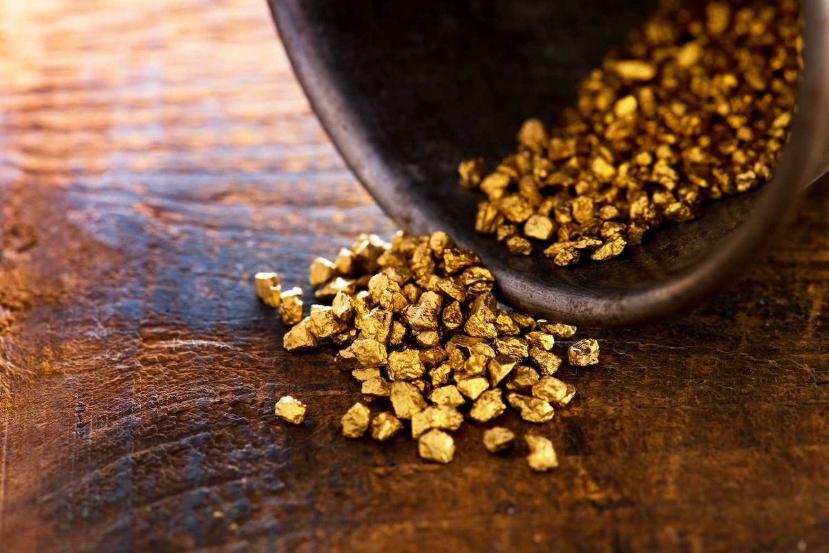 Gold nuggets spilling from a container onto a wooden surface.