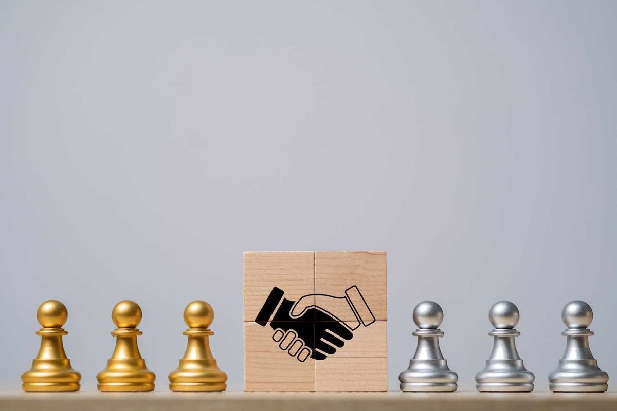 Golden and silver pawns with handshake block in center, symbolizing cooperation.