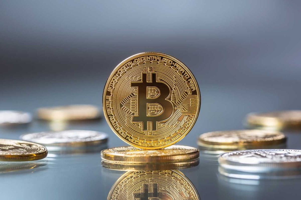 Golden Bitcoin coin standing on reflective surface, with blurred coins in the background.