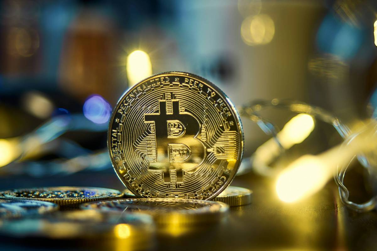 Golden Bitcoin coin stands upright among blurred fairy lights on a dark surface.