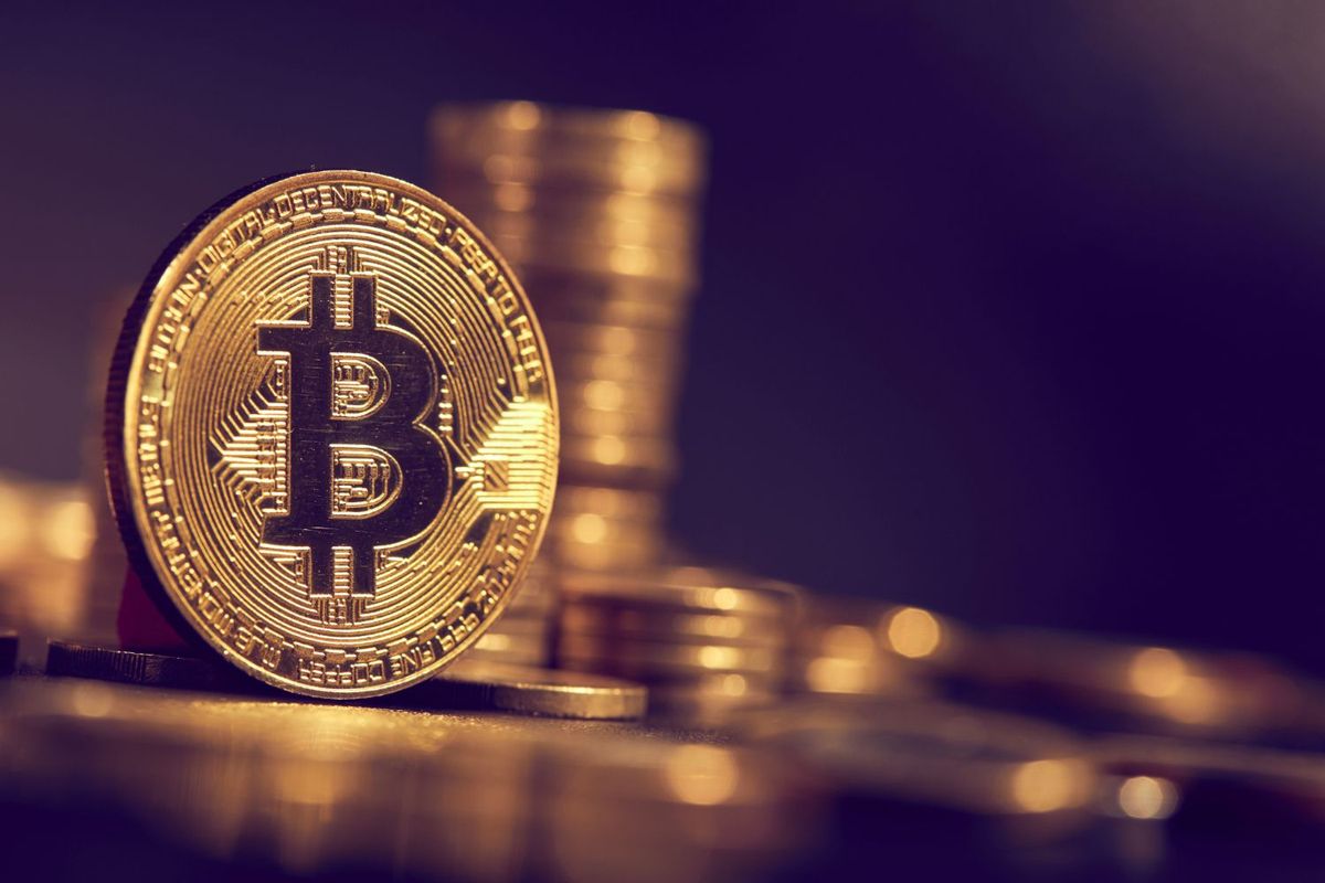 Golden Bitcoin coin with stacks of coins in the background.