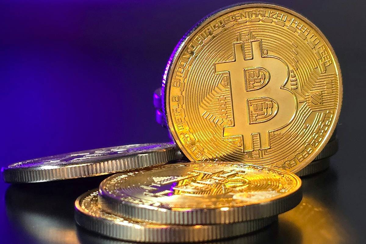 Golden Bitcoin coins stacked against purple background.