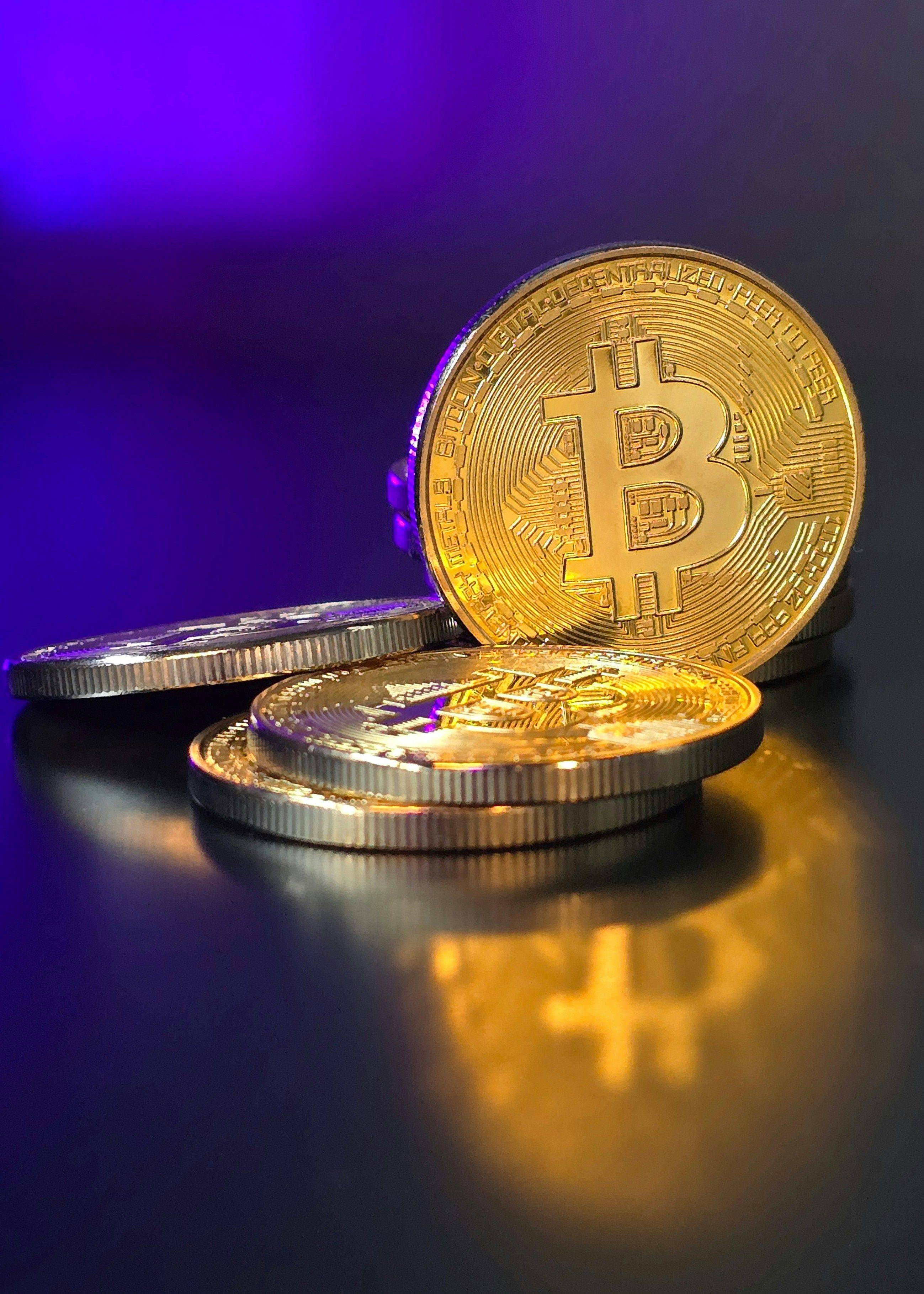 Golden Bitcoin coins stacked against purple background.