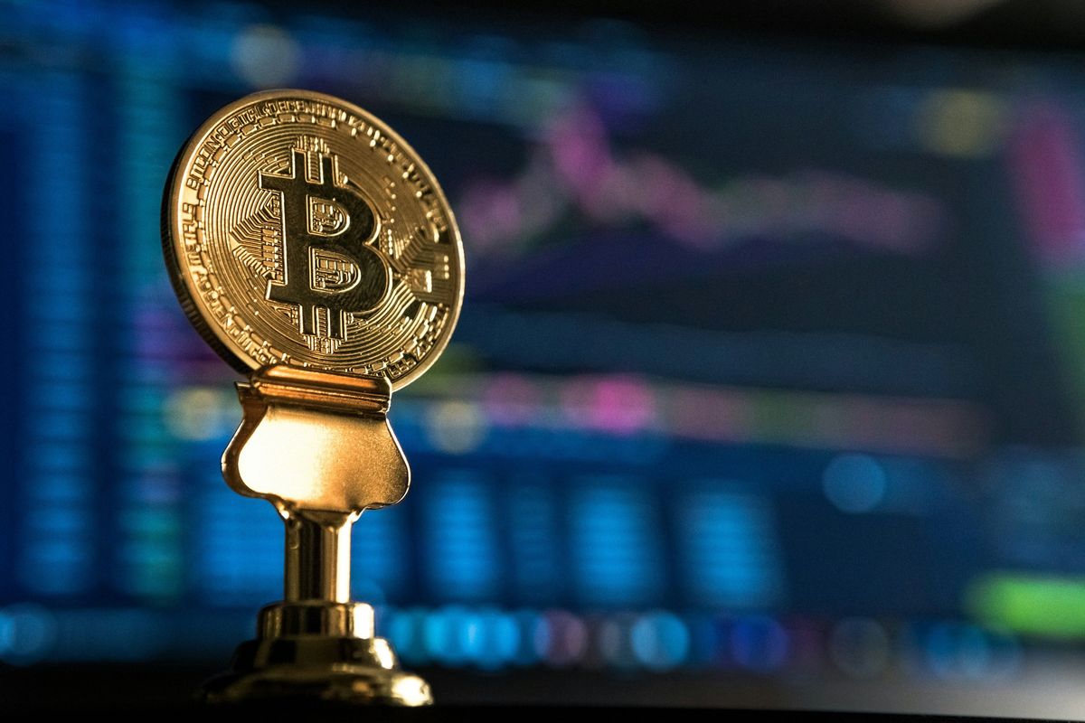 Golden Bitcoin symbol with stock market graph in the background.
