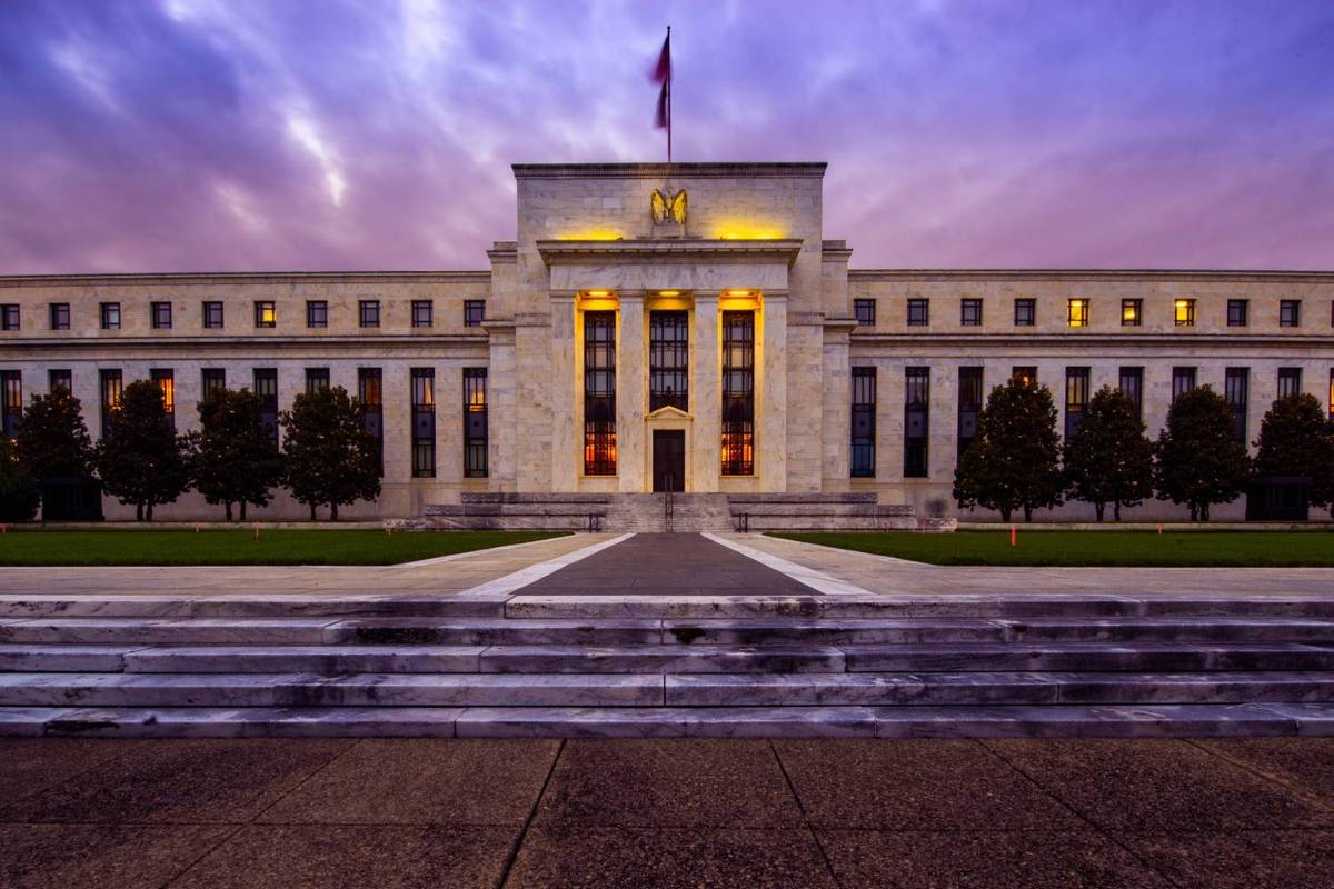 Grand building with columns and flag, lit at twilight against a purple sky.