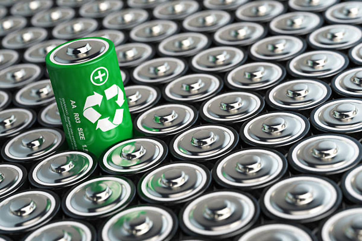 Green battery with recycling symbol among many silver batteries.