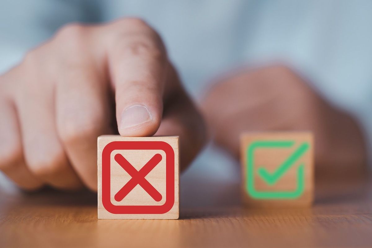 Hand choosing a block with a red X beside a green checkmark block on a table.