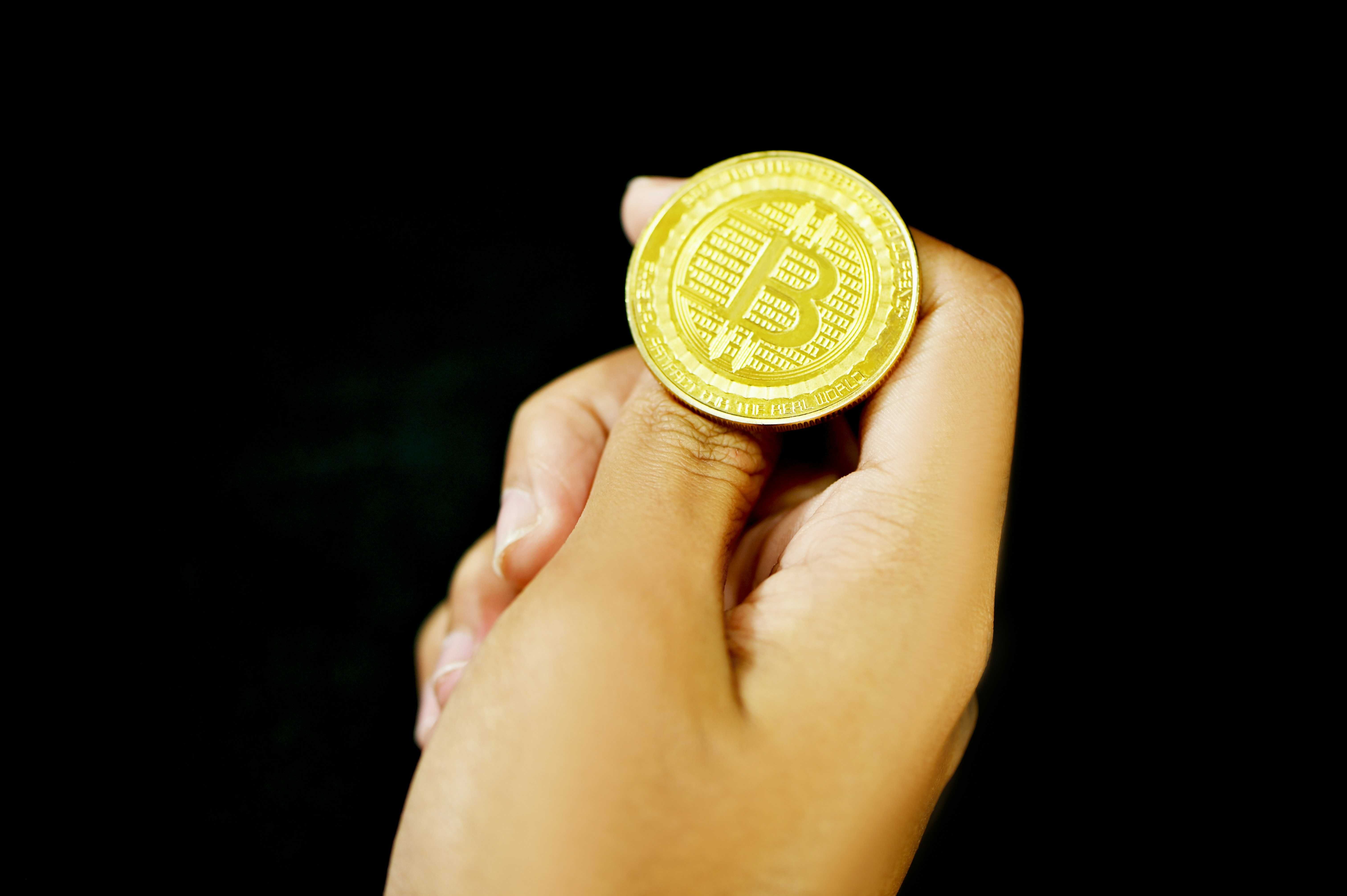 Hand holding a gold Bitcoin coin on a black background.