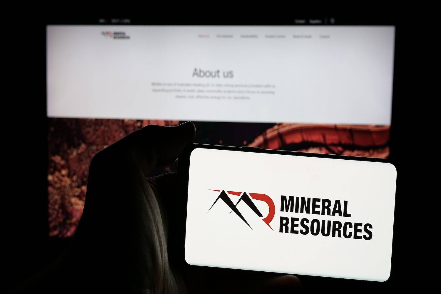 Hand holding a phone displaying Mineral Resources logo.