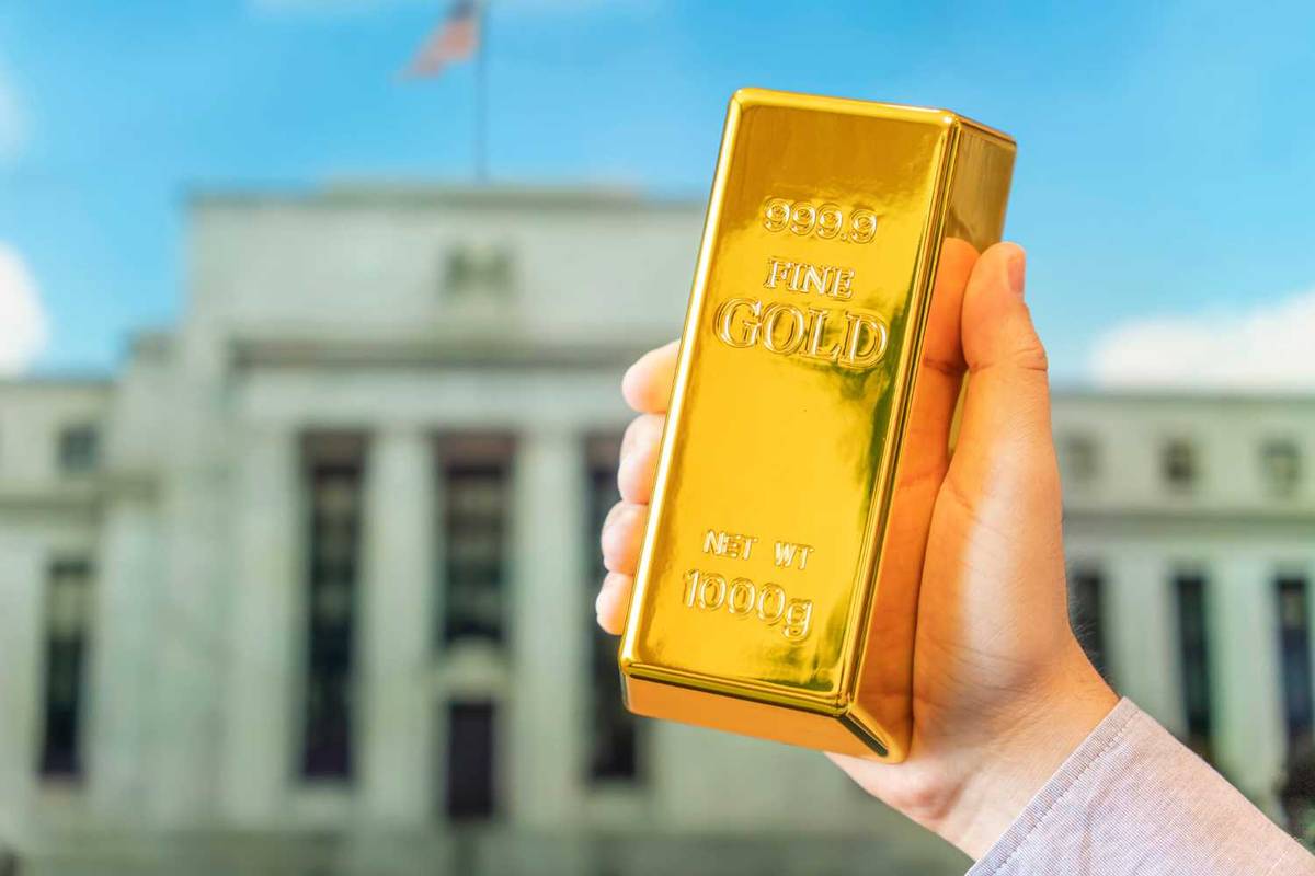 Hand holding gold bar in front of blurred building.