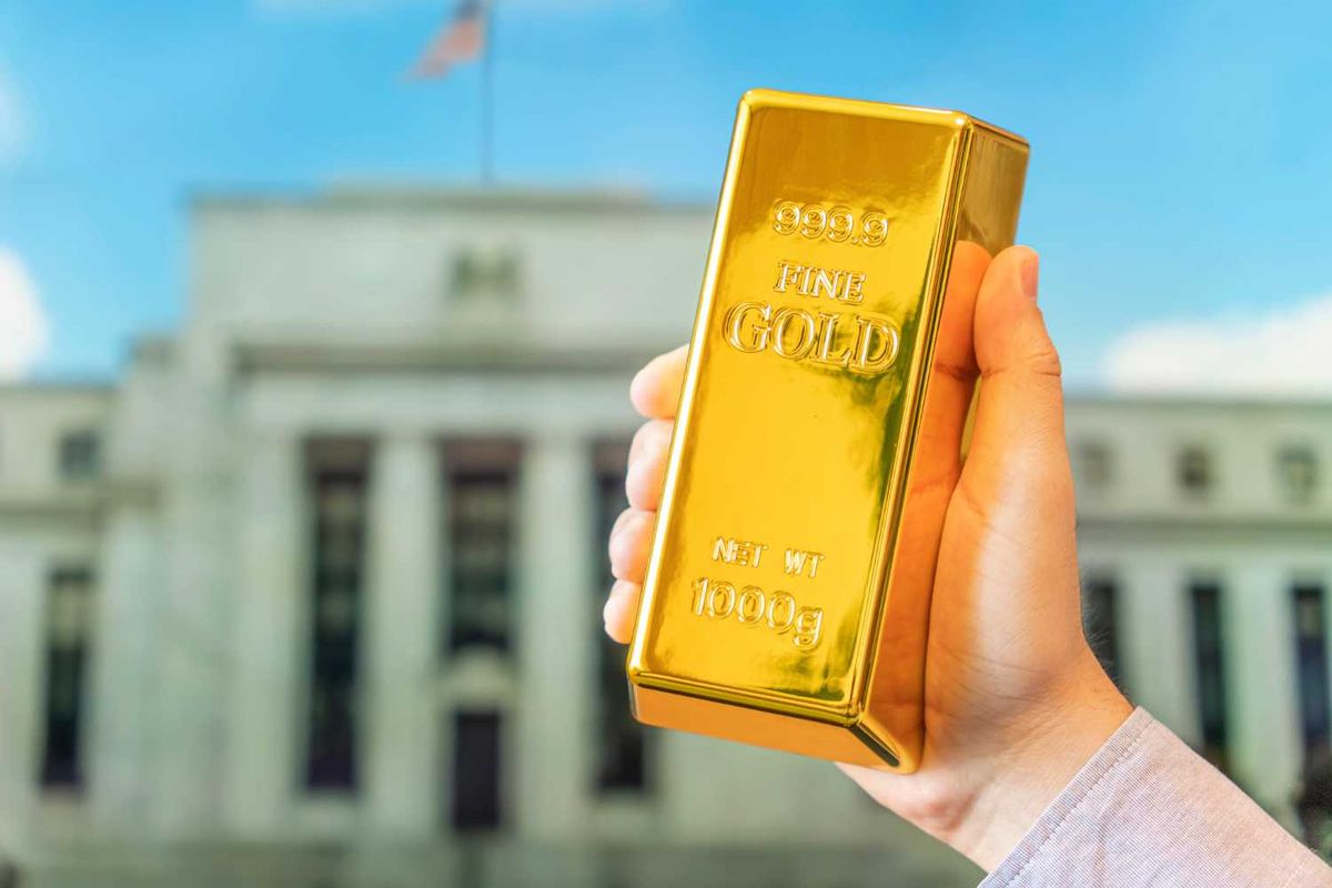 Hand holding gold bar in front of blurred building.