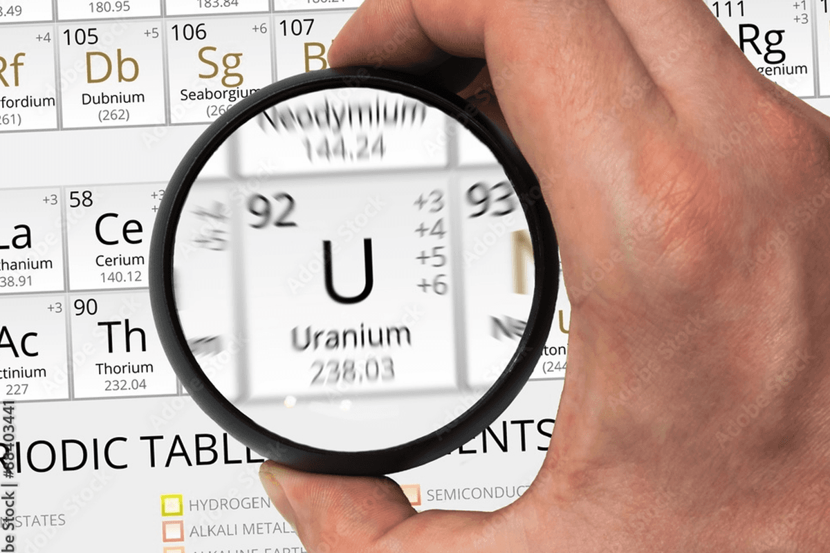 Hand holding magnifying glass over uranium on periodic table.