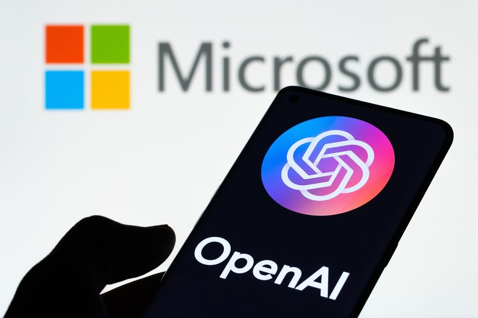 Mano sosteniendo el teléfono con tecnología OpenAI frente al logotipo de Microsoft