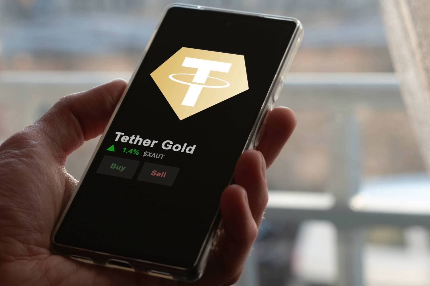 Hand holding smartphone displaying Tether Gold with buy and sell options.