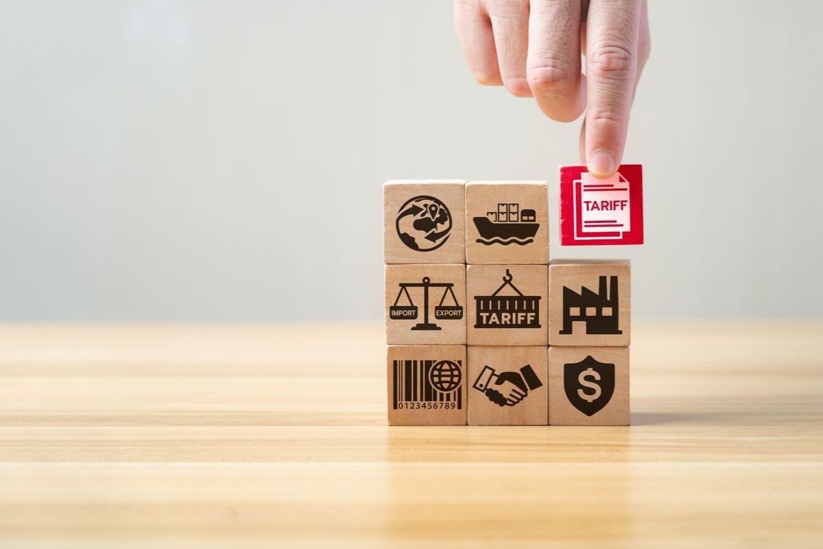 Hand placing a red "tariff" block on stacked wooden trade blocks.