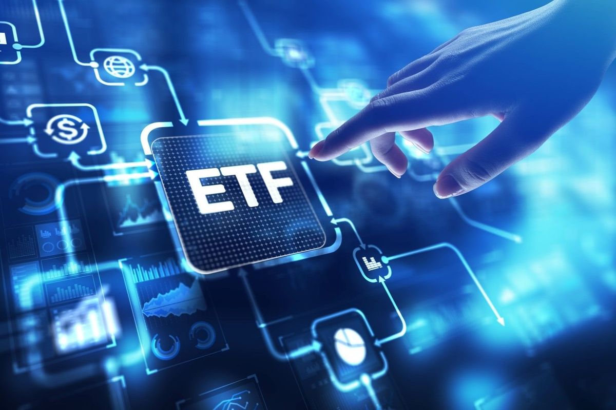 Hand reaches towards blue-toned digital screen with button that reads "ETF" surrounded by stock-related chart imagery.