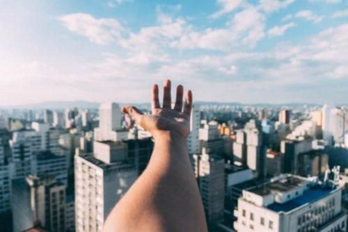 hand reaching out against backdrop of buildings