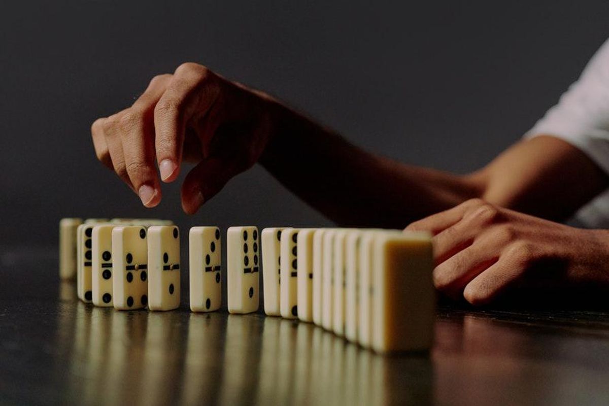 hand reaching to pick up one domino in a line of dominos